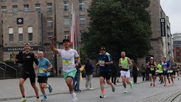 Marathon-Läufer beim 41. Rhein-Ruhr-Marathon. Ganz vorne ein Mann in weißem Shirt und grüner Hose, der in die Kamera lächelt.