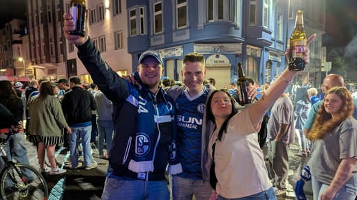 Zwei Männer und eine Frau bejubeln den Aufstieg von Schalke 04