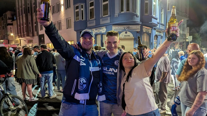 Zwei Männer und eine Frau bejubeln den Aufstieg von Schalke 04