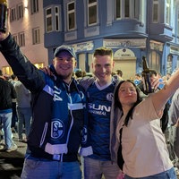 Zwei Männer und eine Frau bejubeln den Aufstieg von Schalke 04