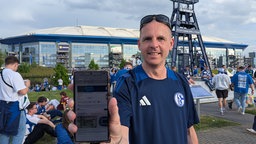 Schalke-Fan Sascha Walmsley zeigt stolz das Ticket, dass er geschenkt bekommen hat.