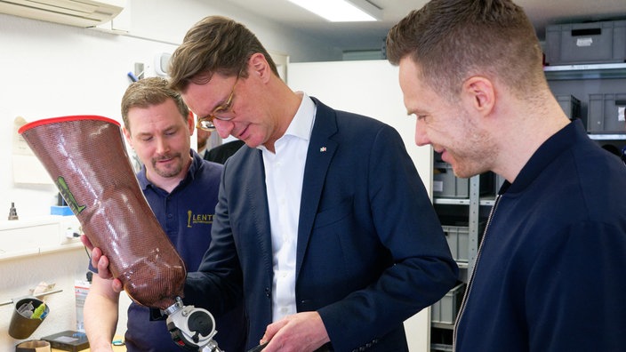 Henrik Wüst zusammen mit dem Weitspringer Markus Rhem (r.), bei Orthopädietechnikermeister Tim vom Hagen (l.) bei einem Besuch des Bundesstützpunktes Para-Leichtathletik in Leverkusen