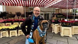 Ein Mann lächelt in die Kamera, neben ihm sein Hund.