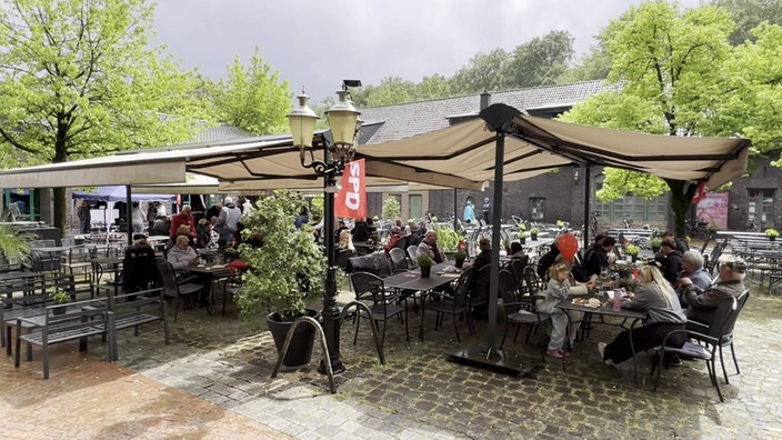 Das SPD-Treffen während Regen: Menschen sitzen unter großen Schirmen zusammen