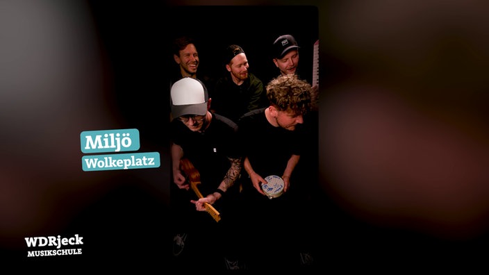 Die Band sitzt in einem engen Studio und spielt auf Kinderinstrumenten