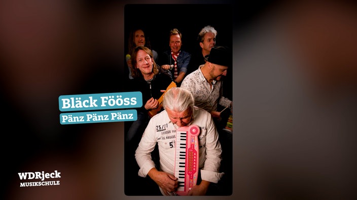 Die Band sitzt in einem engen Studio und spielt auf Kinderinstrumenten