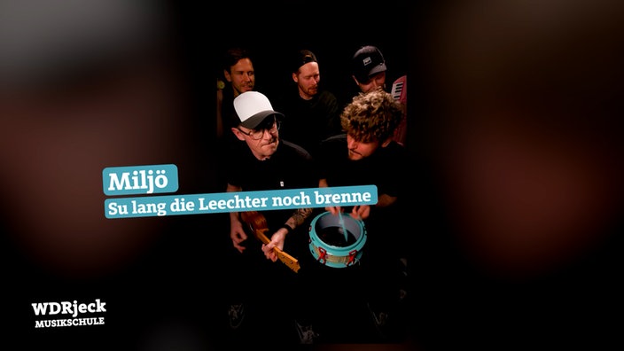 Die Band sitzt in einem engen Studio und spielt auf Kinderinstrumenten
