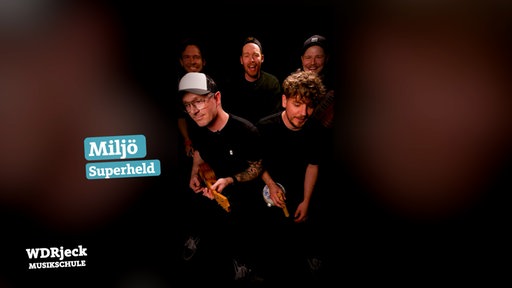 Die Band sitzt in einem engen Studio und spielt auf Kinderinstrumenten