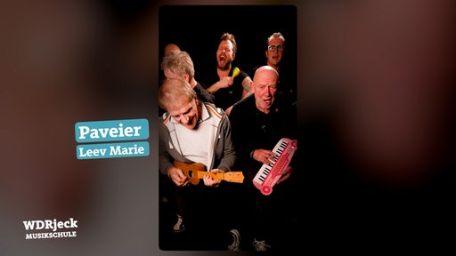 Die Band sitzt in einem engen Studio und spielt auf Kinderinstrumenten
