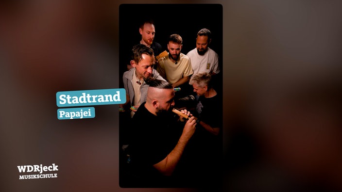 Die Band sitzt in einem engen Studio und spielt auf Kinderinstrumenten