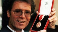 Cliff Richard präsentiert vor dem Buckingham-Palast seinen Orden, den er kurz vorher von Königin Elizabeth II. erhalten hatte, als sie ihn zum Ritter schlug