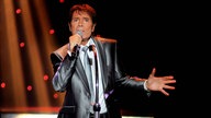 Cliff Richard mit Mikrofon in der Hand, singend, auf der Bühne