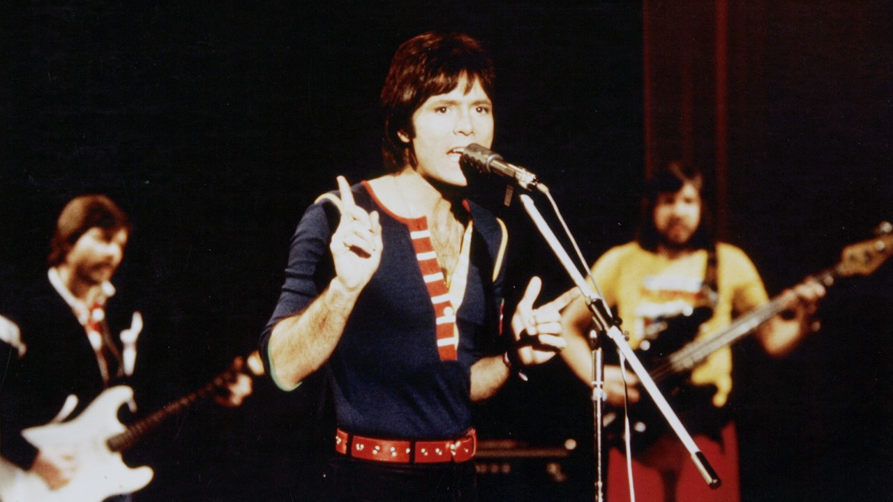 Cliff Richard steht auf der Bühne am Mikro und singt