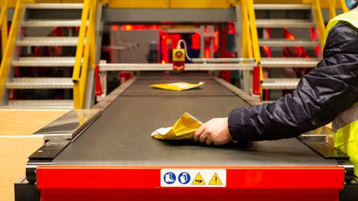 Eine Männerhand legt ein flaches Päckchen auf ein Fließband