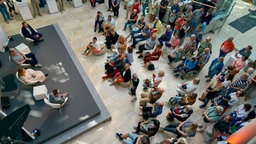 Menschen sitzen und stehen im Foyer und verfolgen eine Podiumsdiskussion