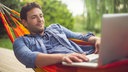 Junger Mann mit Laptop liegt in Hängematte