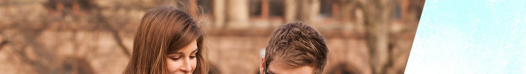 Zwei junge Menschen sitzen auf einer Bank und schauen in einen Ordner