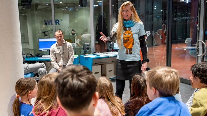 Ein Frau trägt ein Maus-T-Shirt und spricht vor einer Kindergruppe