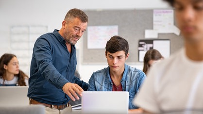 Lehrer neben Schüler am Rechner