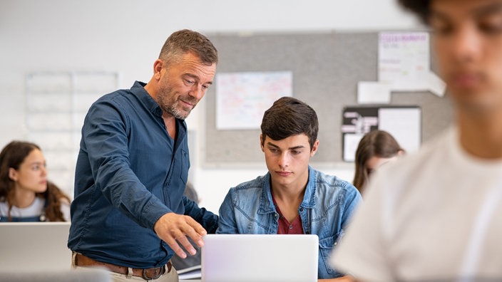 Lehrer neben Schüler am Rechner