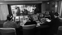 Schwarz-Weiß-Bild: Blick aus einer Fernsehregie in ein Fernsehstudio
