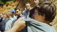 Filmszene, Junge wir am Kragen gepackt, Männer im Hintergrund