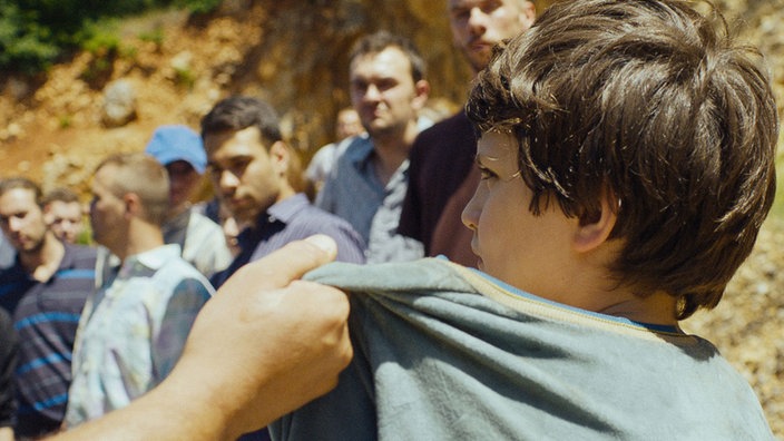 Filmszene, Junge wir am Kragen gepackt, Männer im Hintergrund
