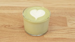 Ein Glas mit Matcha Latte auf einem Holztisch