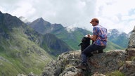Auf dem Bild sieht man Franz Alken auf einem Felsen beim Zeichnen.