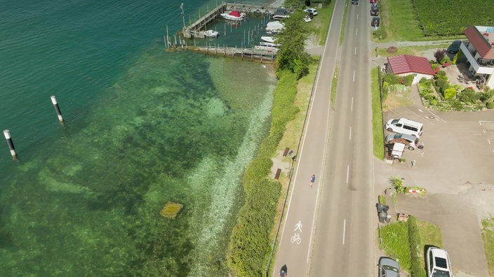 Blick von oben auf Straße mit breitem Radweg neben dem Seeufer