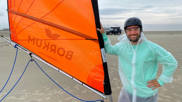 Daniel Aßmann mit Helm hält das Segel eines Strandseglers