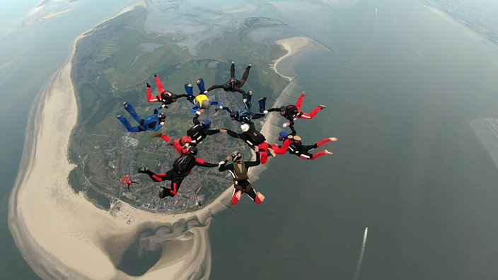 Mehrere Fallschirmspringer bilden einen Ring über der Insel Borkum