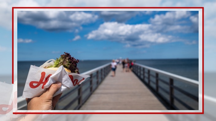 Ein Fischbrötchen in der Hand, im Hintergrund die Seebrücke Ahlbeck