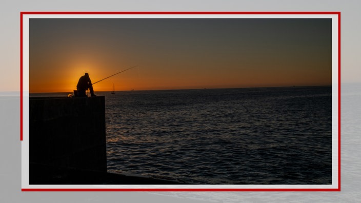 Angler sitzt auf einer Kaimauer im Sonnenuntergang