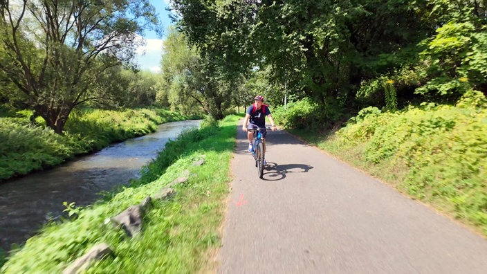 André Gatzke fährt mit dem Fahrrad auf einem Radweg neben einem Flüsschen