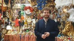  Tobia Dall’Osto steht in seiner Maskenwerkstatt vor einer Wand mit vielen Masken