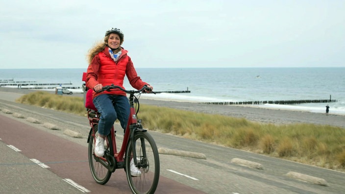 Tamina Kallert fährt mit dem Fahrrad auf einer Sgtraße entlang der Küste