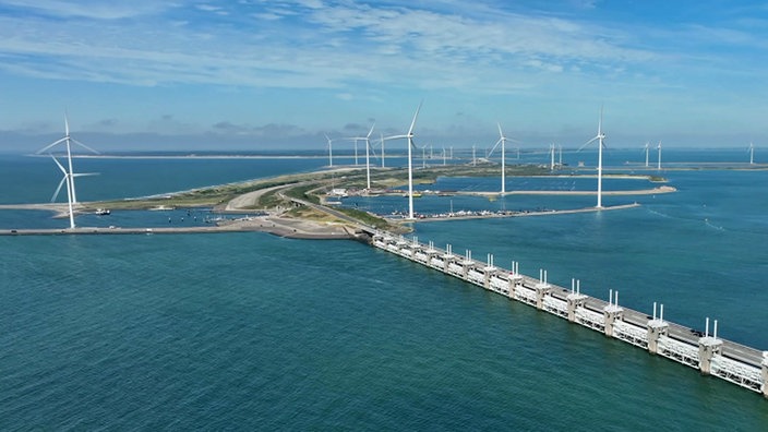 Luftaufnahme vom Sturmflutwehr der Oosterscheldekering, dahinter mehrere Windräder