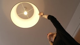 Eine Frau greift nach oben an eine Deckenlampe