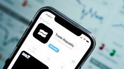 Ein Smartphone vor einem Laptop-Bildschirm. Auf dem Smartphone ist die Trade Republic Startseite im Apple Store zu sehen
