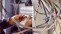 Das Bild zeigt einen Sicherungskasten, an dem ein Handwerker arbeitet. 