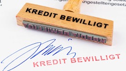 Ein Stempel aus Holz liegt auf einem Dokument mit der Aufschrift "Kredit bewilligt".