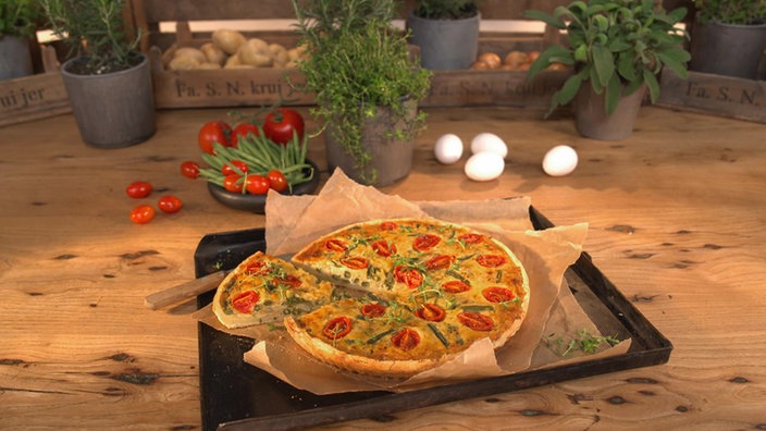 Das Bild zeigt die Quiche garniert mit Tomaten und Bohnen auf einem Backblech.