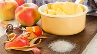 Zubereitung von Apfelmus: Ungeschälte und geschälte Äpfel in einem Topf mit Zucker 