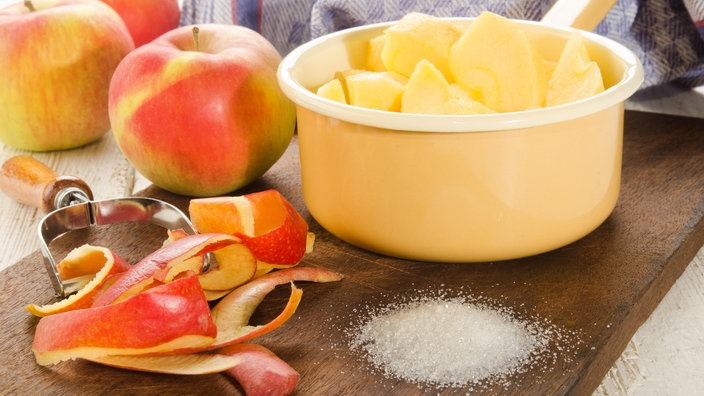 Zubereitung von Apfelmus: Ungeschälte und geschälte Äpfel in einem Topf mit Zucker 