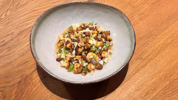 Ein Teller mit „Blumenkohl-Ceviche mit Rauchmandeln“ steht auf einem Holztisch.