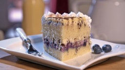 Heidelwitzka Torte mit Heidelbeeren wird auf einem weißen Teller mit einer Gabel präsentiert