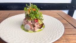 Auf einem weißen Teller ist "Sylter Krabbenbrot" angerichtet – mit Krabben, Senfsauce und Wildkräutersalat.