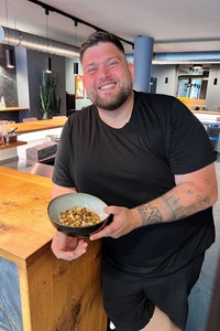 Lukas Jacobi steht in seinem Restaurant, mit breitem Grinsen und einem Teller seiner Ceviche in der Hand.