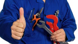 Das Bild zeigt einen Handwerker mit Werkzeug, der mit dem Daumen nach oben zeigt. 